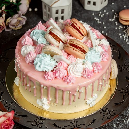 pink cream drip cake garnished with pink and blue creams and macaroons